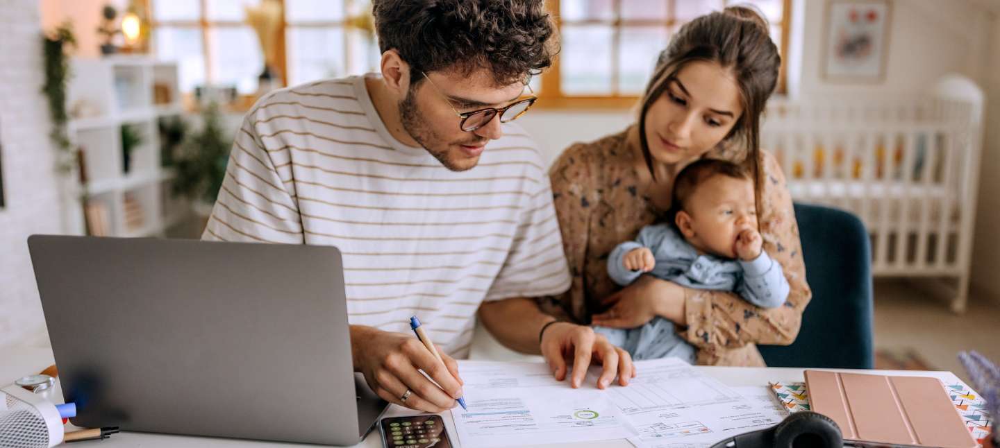 Parents reviewing their budget at home while holding their baby.