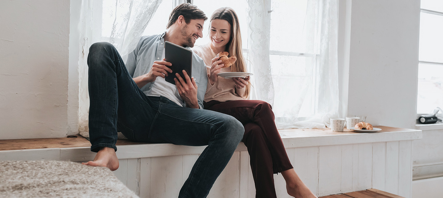 couple sitting in home looking at a tablet and having breakfast