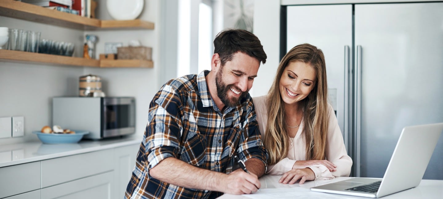Smiling man and woman looking over mortgage and financial documents sitting at kitchen table.