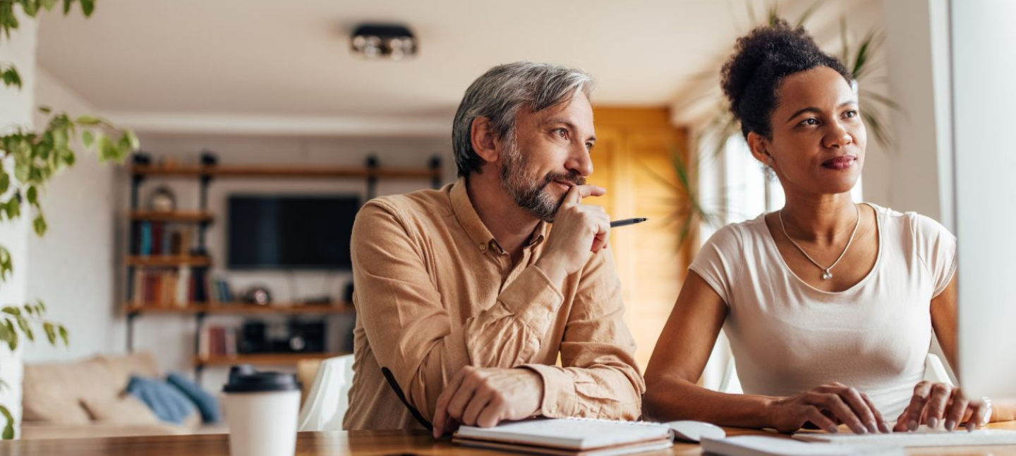 A man and woman working on a laptop at their kitchen counter at home.