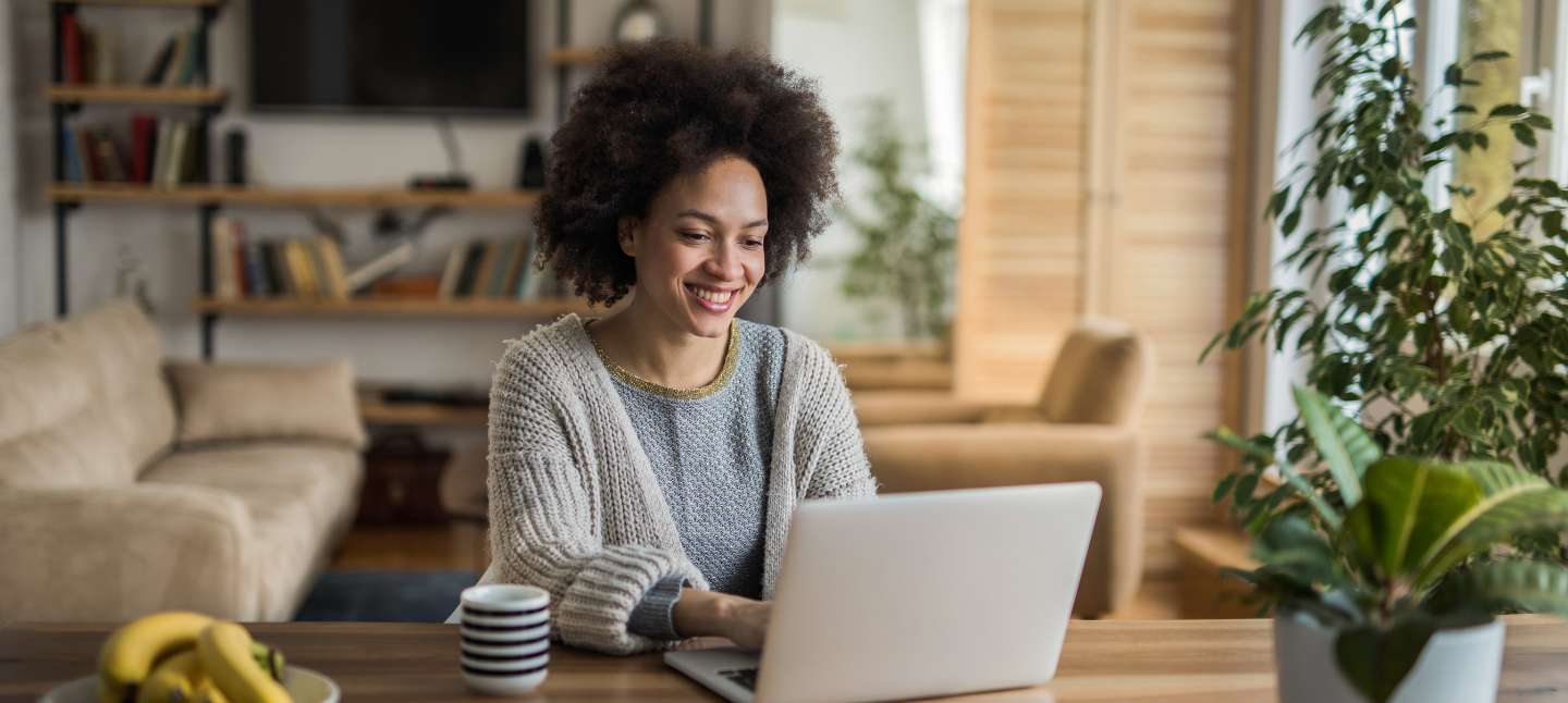 Young happy African American woman using laptop and at the kitchen table.