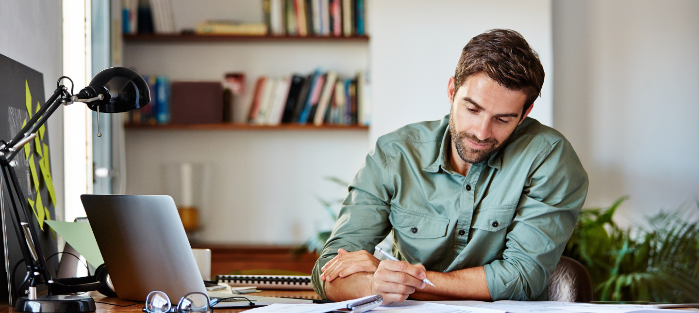 Young man sitting at a table at home working on a laptop.
