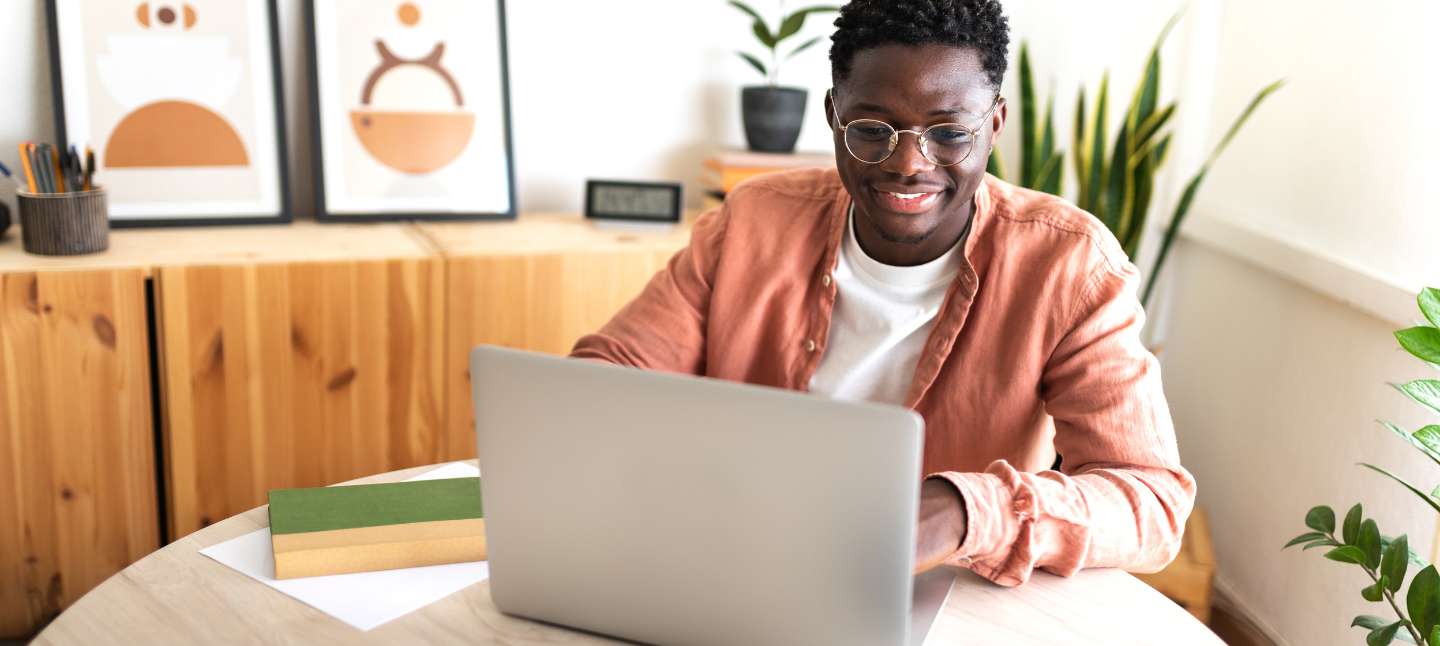 Happy black male university student studying at home using laptop.