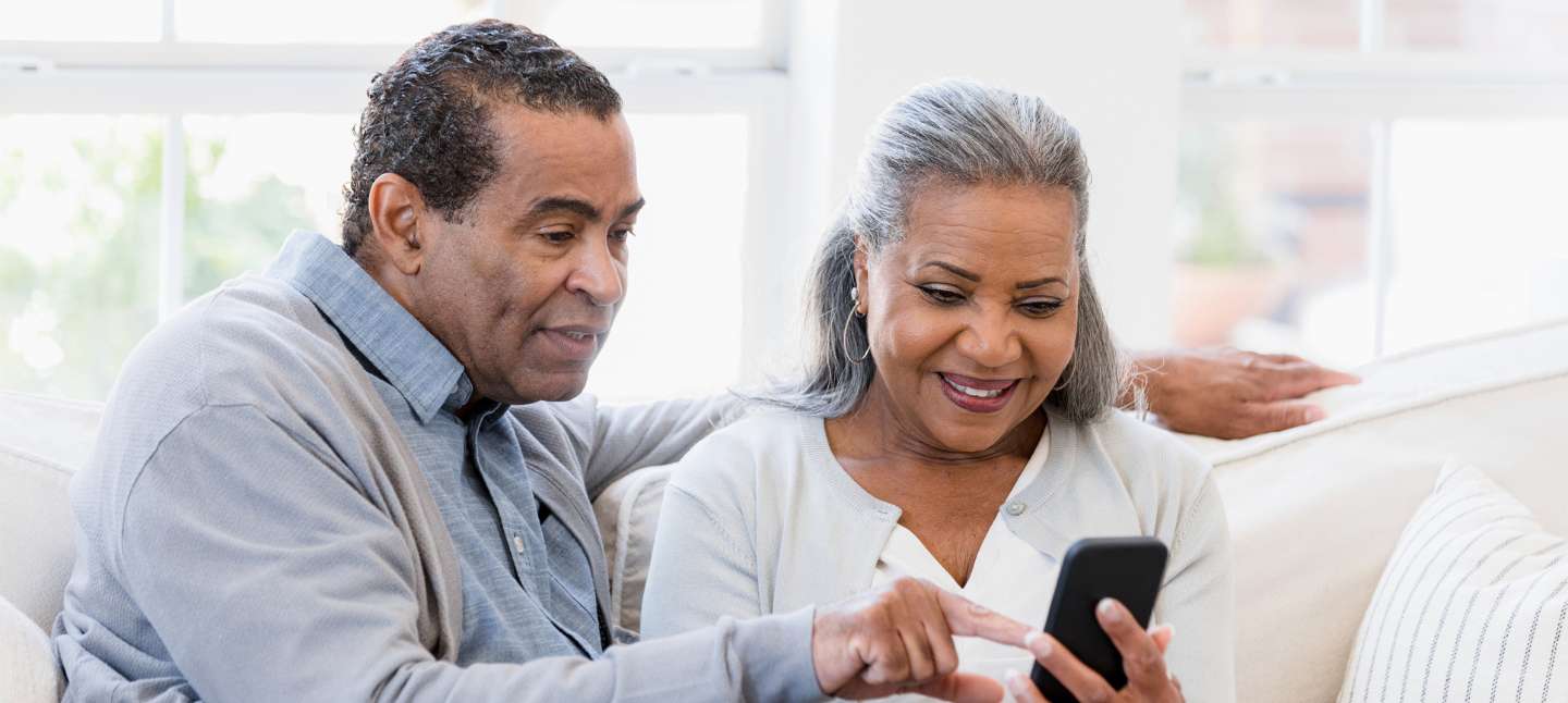 Husband and wife sitting on the couch and managing their finances on the phone.