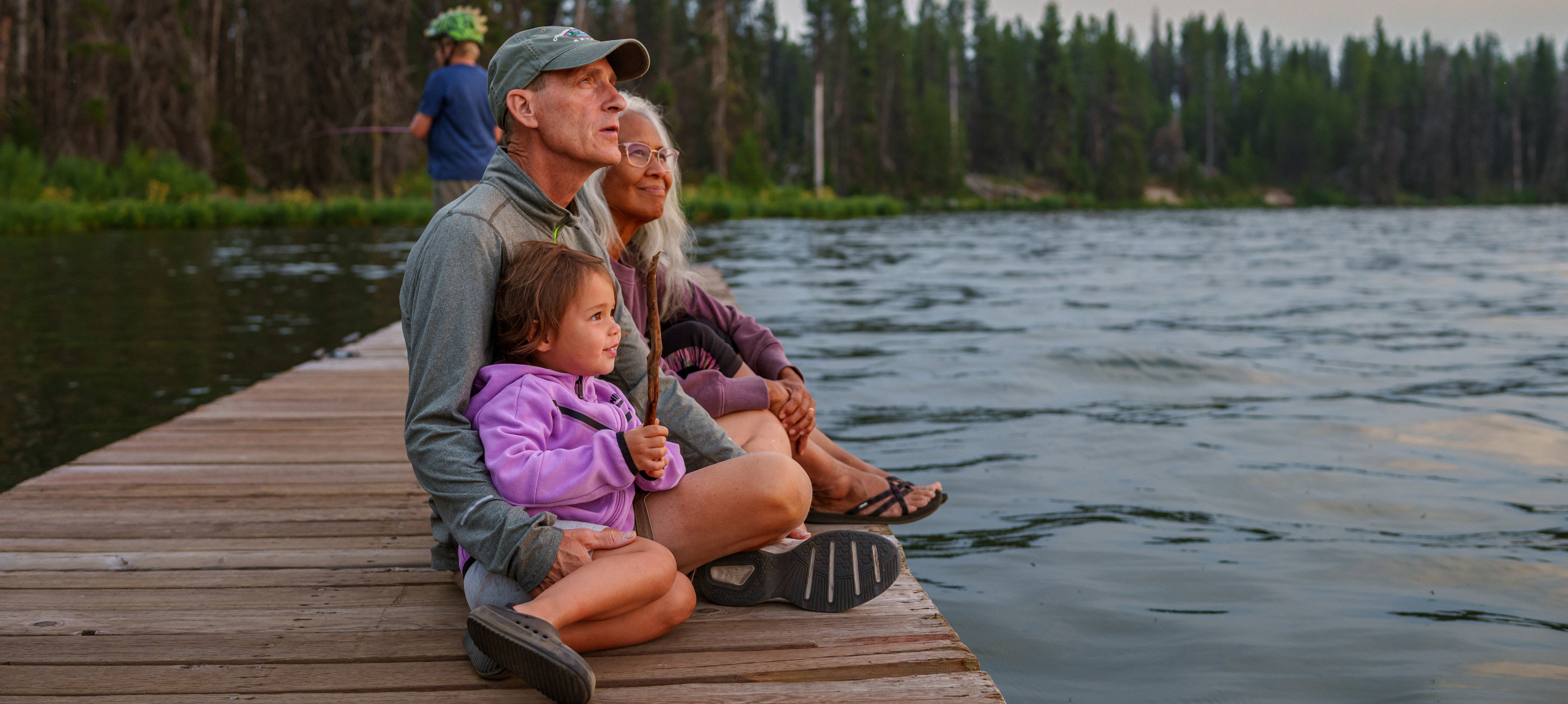 Grandparents and granddaughter enjoy sunset on a lake dock
