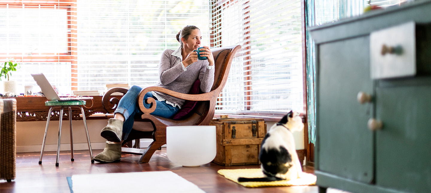 A woman drinking tea looking out the window with her cat