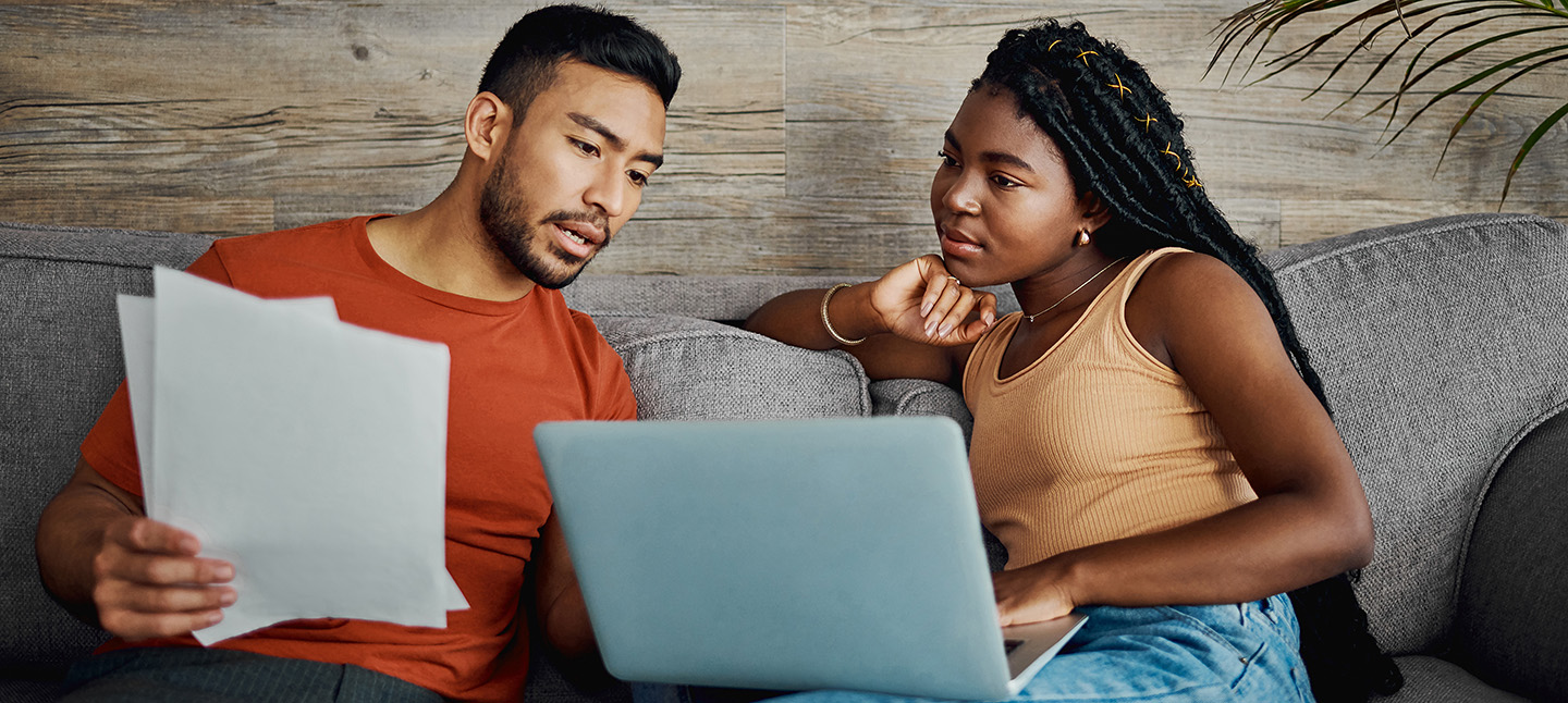 a young couple sitting in the living room at home and using a laptop to calculate their finances