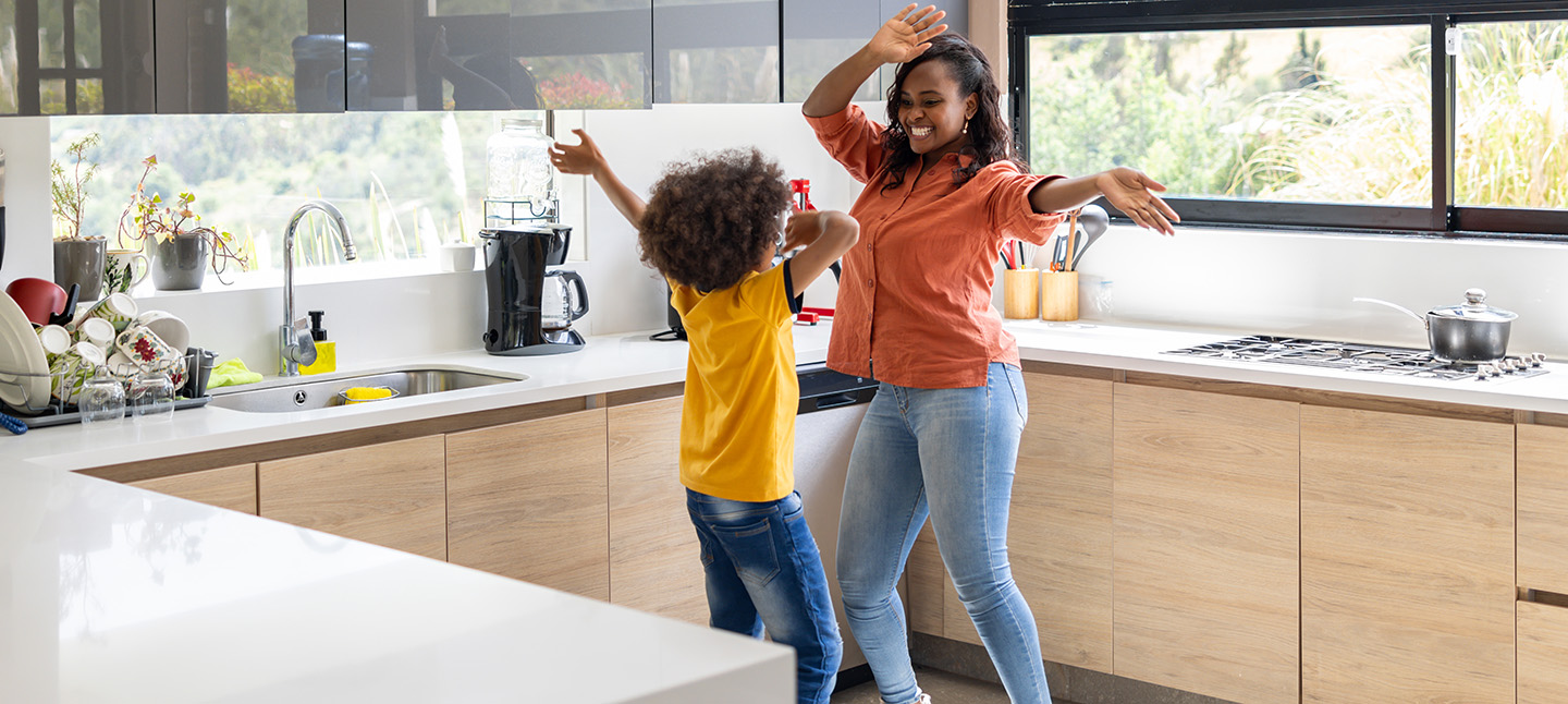 Happy mother and son dancing together at home in the kitchen