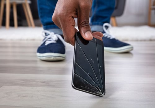 Image of a hand picking up an iPhone with a cracked screen off of the floor